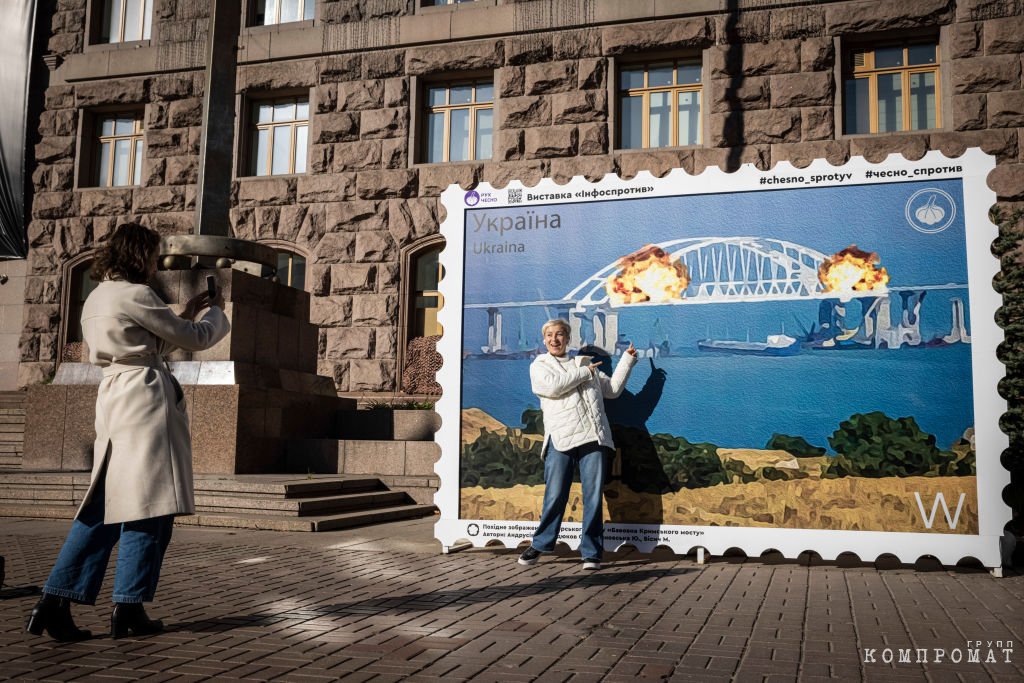 Люди позируют перед изображением почтовой марки, на которой изображён горящий Керченский мост, 8 октября 2022 года в центре Киева,